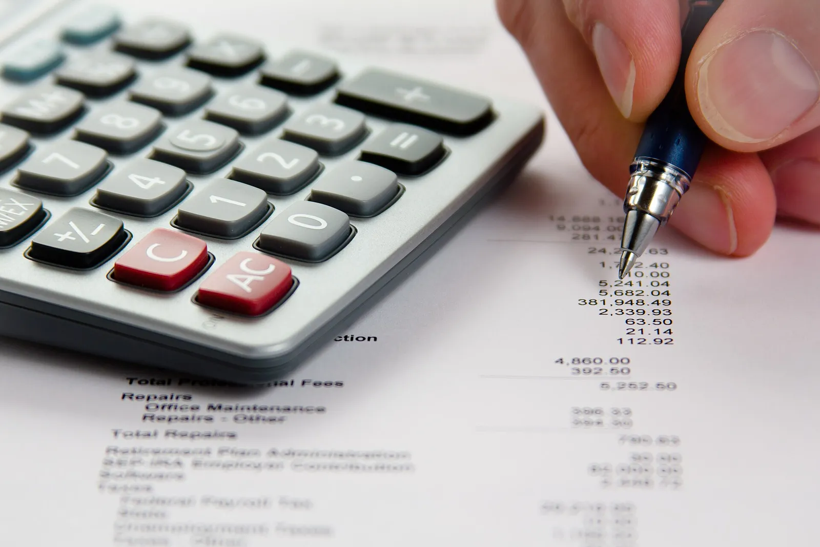 Hand with pen checking a financial statement beside a calculator
